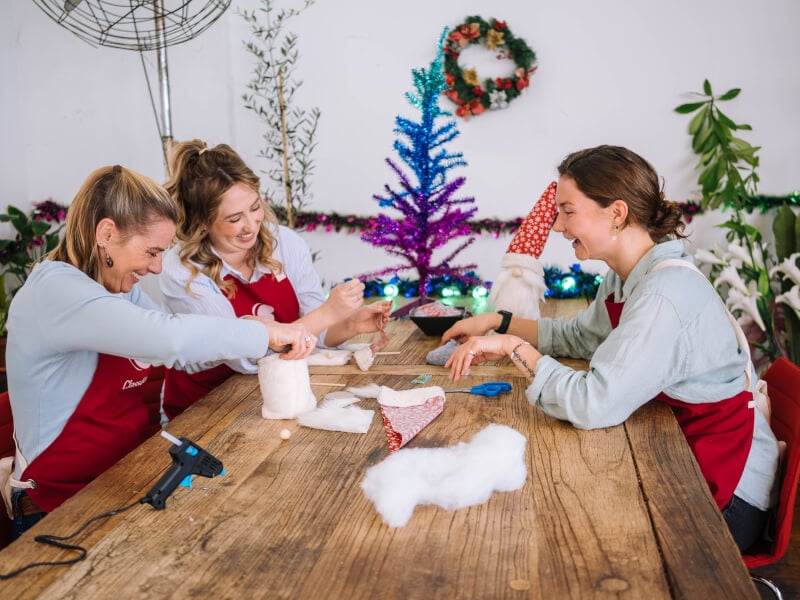 Three women wearing aprons making DIY Christmas crafts